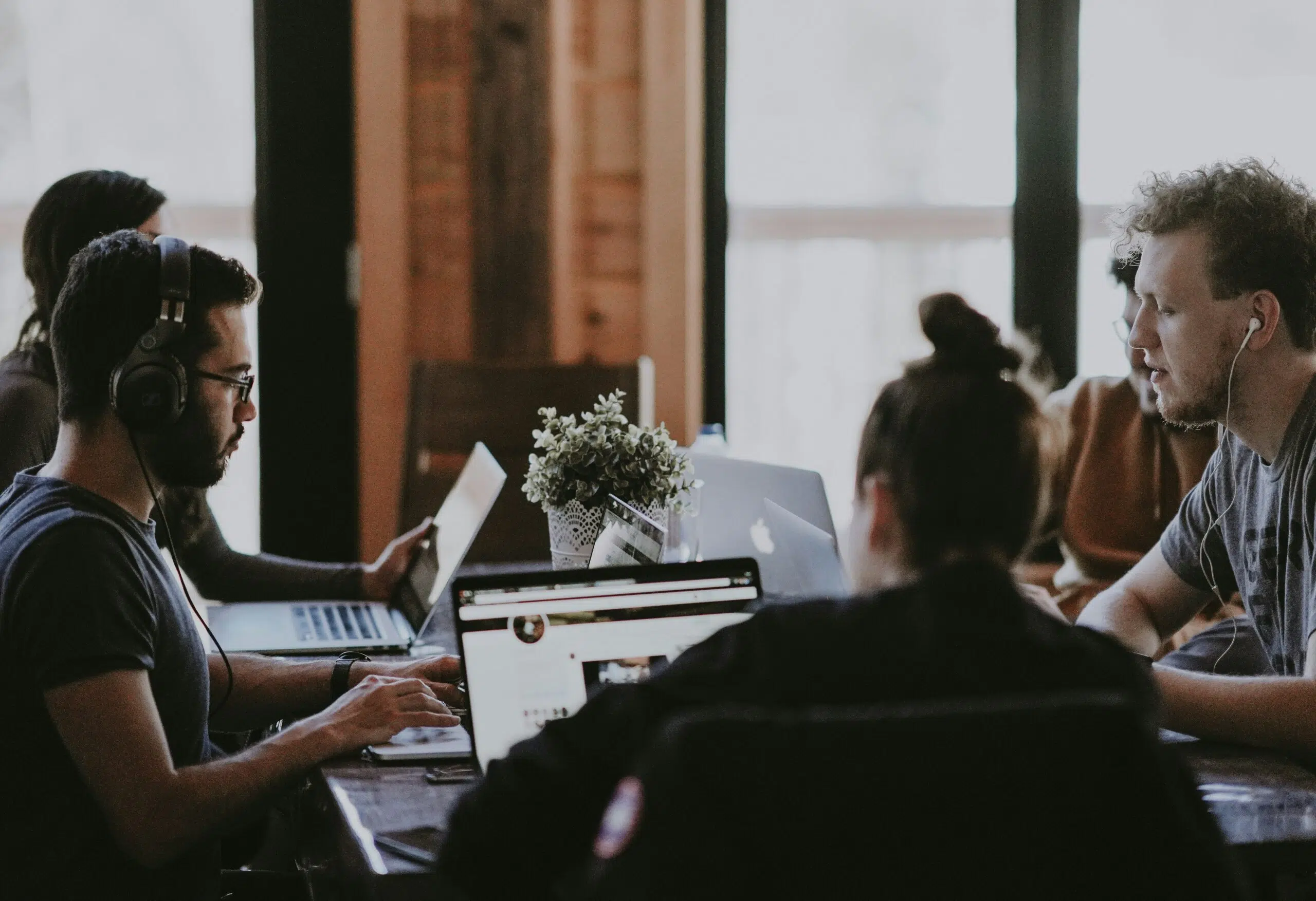 A group of professionals collaborating at a shared workspace, working on laptops and engaged in discussion.