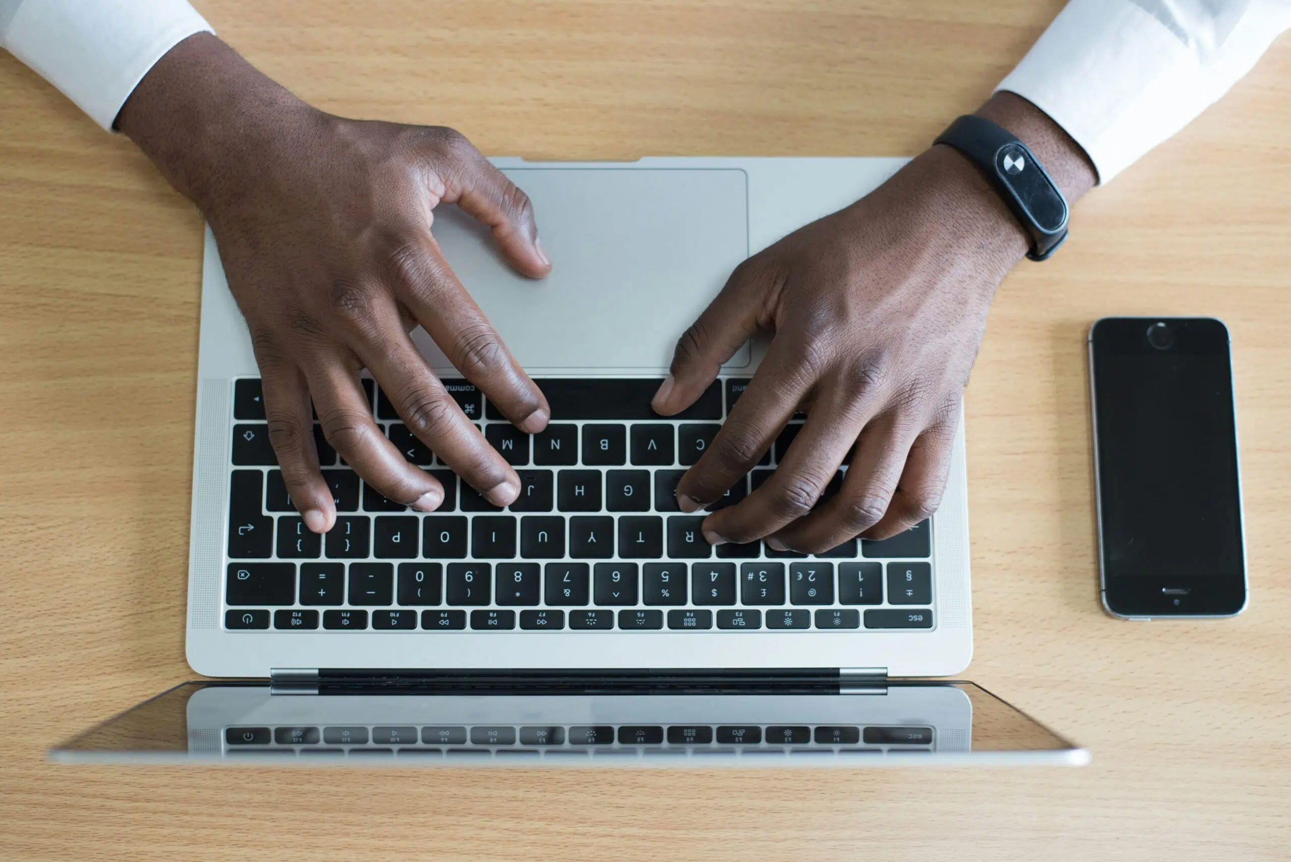 Close-up of hands typing on a laptop keyboard, with a smartphone placed nearby