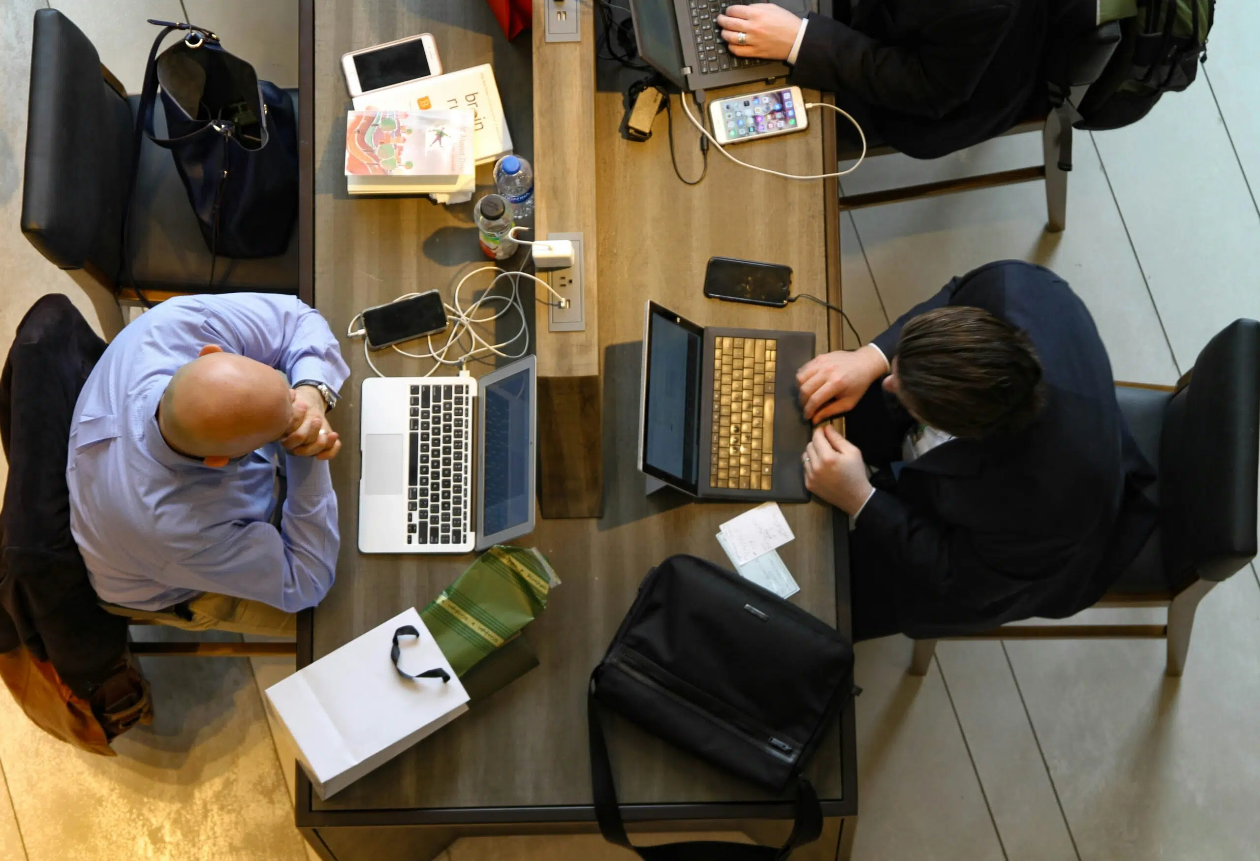 Overhead view of two professionals working on laptops at a shared table with financial documents and books.