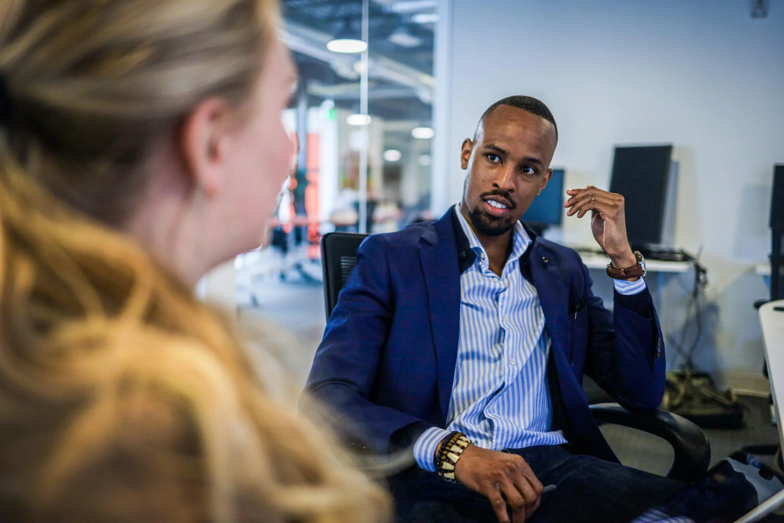 A business professional in a navy suit having a discussion with a colleague in an office setting.