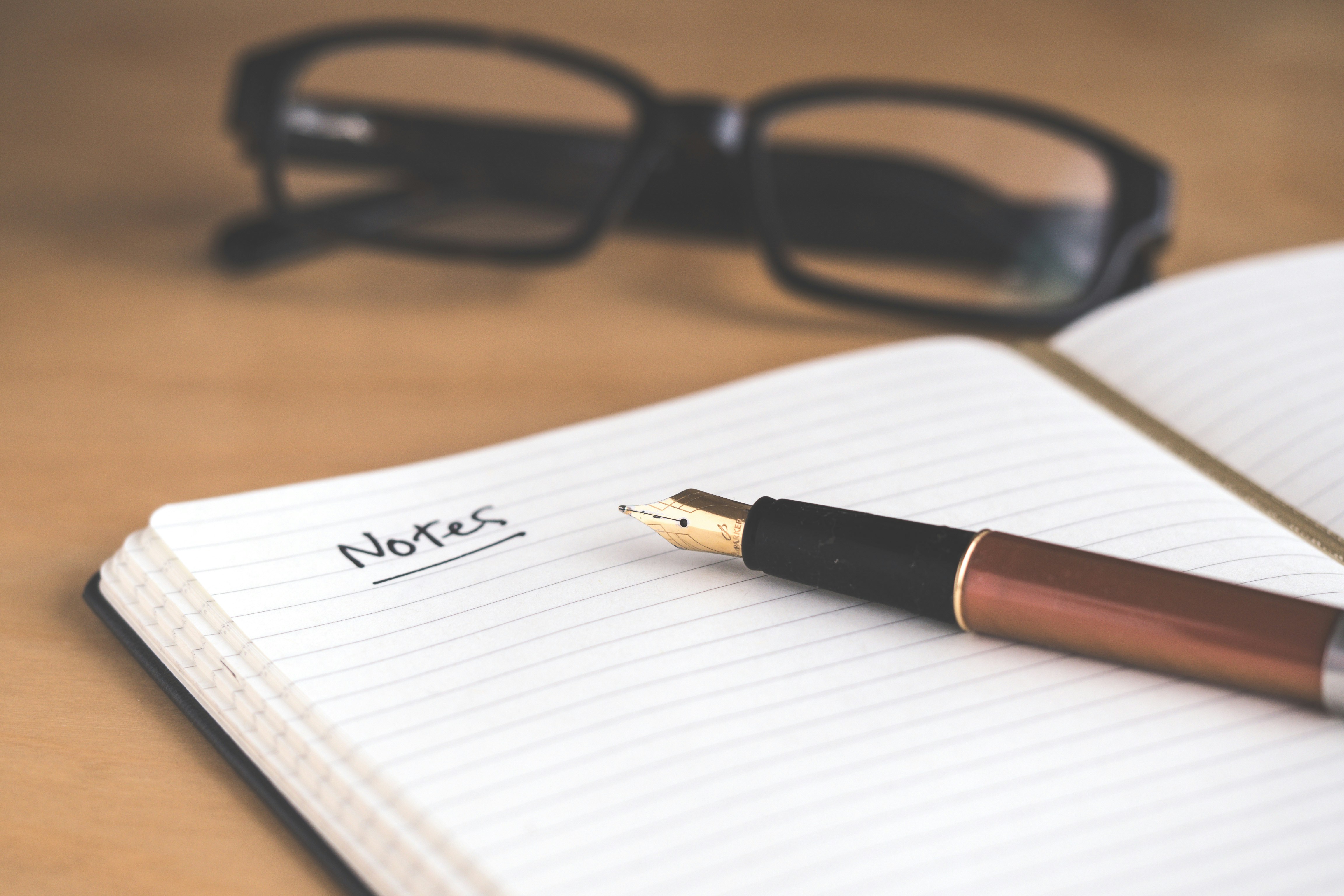 a notebook, pen and glasses on a desk