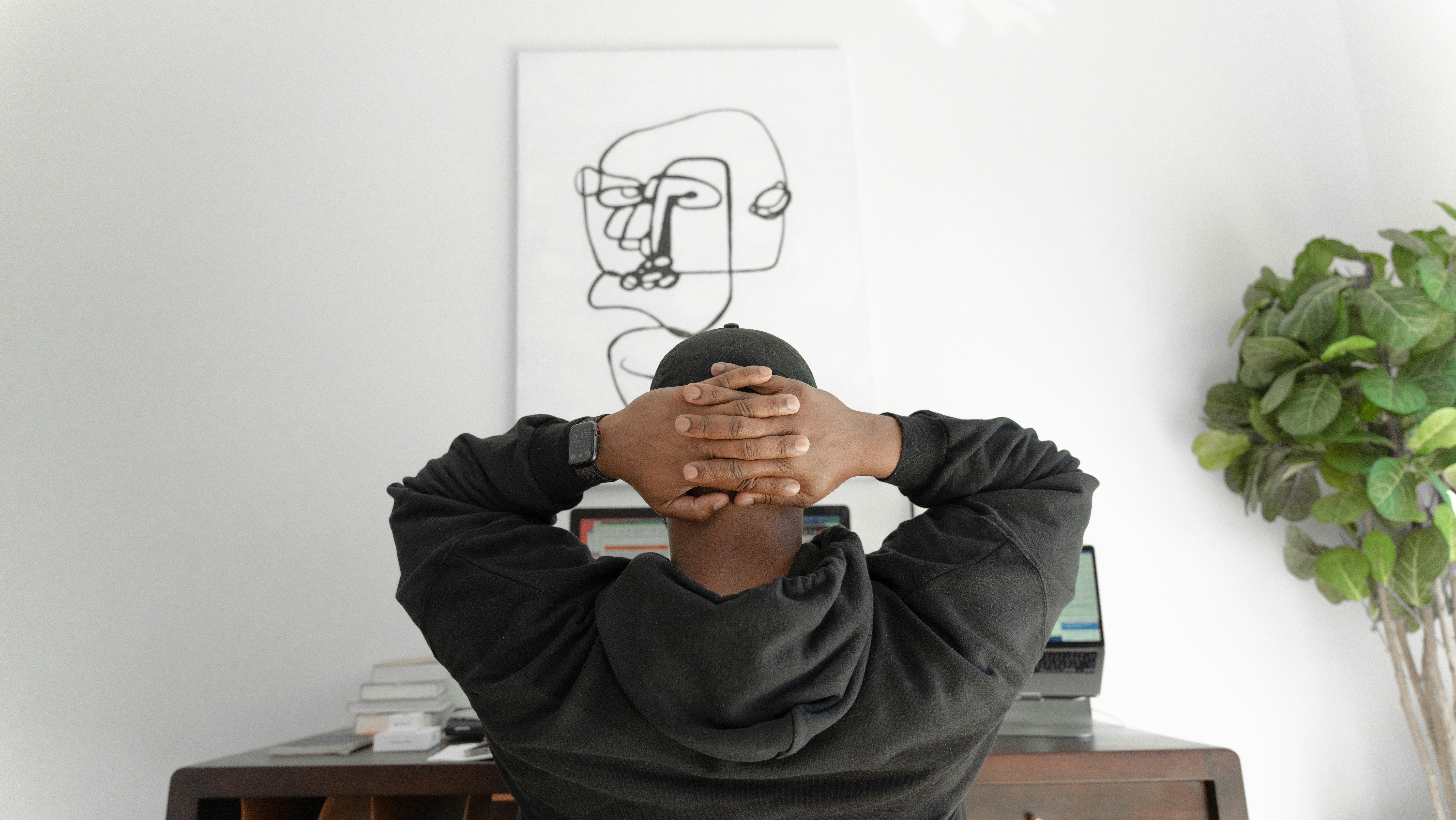 A person sitting at a desk with hands behind their head, reflecting on startup financial challenges in a home office setting. | Cohesion A person sitting at a desk with hands behind their head, reflecting on startup financial challenges in a home office setting.